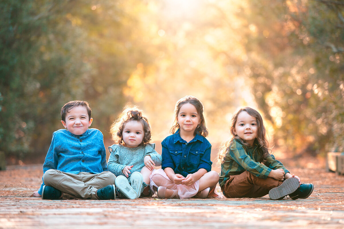 Family photographer Hampton Roads va photograph sibling pictures with for young children sitting together on a bridge in a park while wearing coordinating outfits