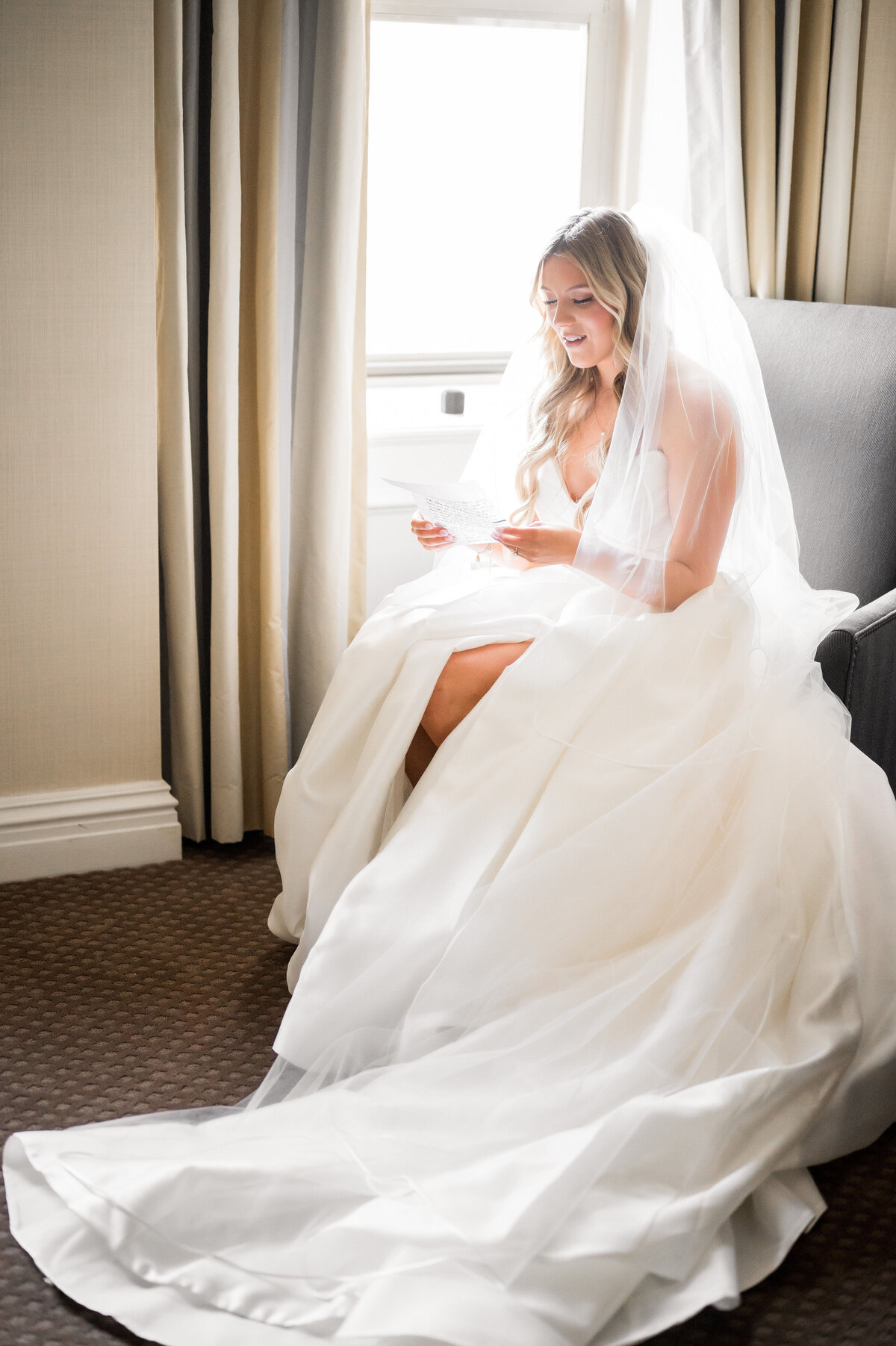 bride reading a letter from the groom on the wedding day in window light of presidential suite of omni william penn pittsburgh