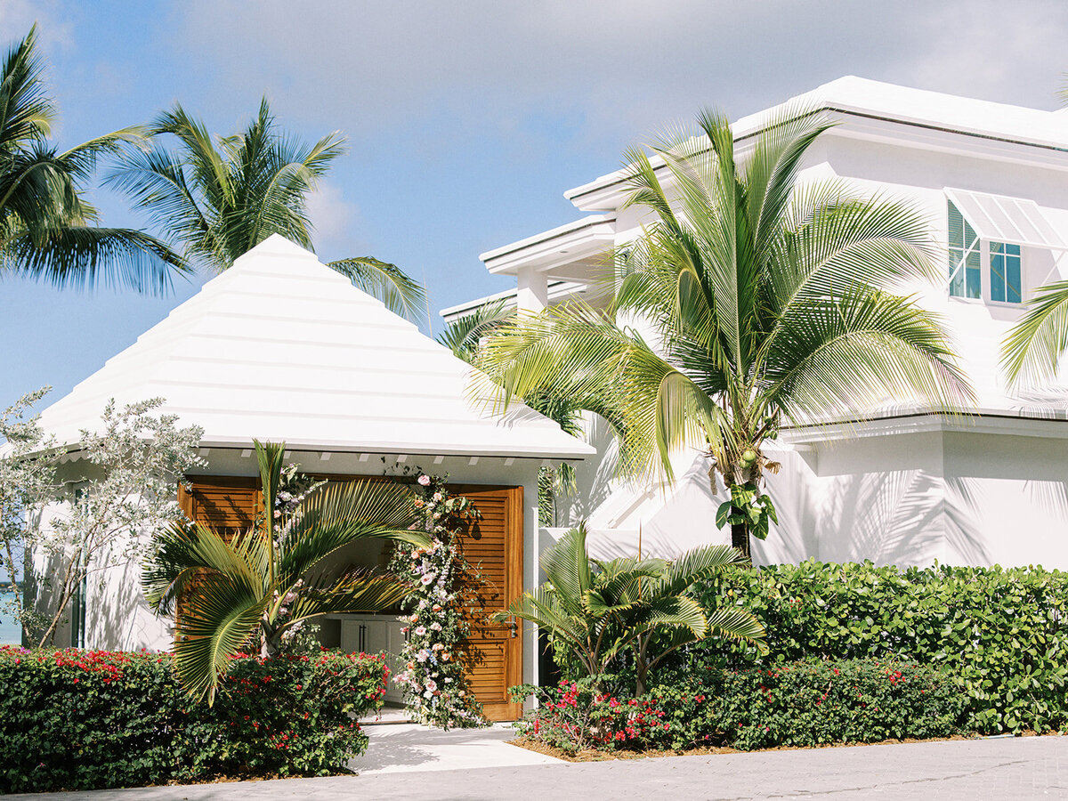 Gate and gatehouse tropical column floral installation for destination spring destination beach wedding in Exuma, Bahamas. Orchids and roses in tropical colors of orange, pink, lavender, dusty blue pale yellow and natural greens. Design by Rosemary & Finch Floral Design.