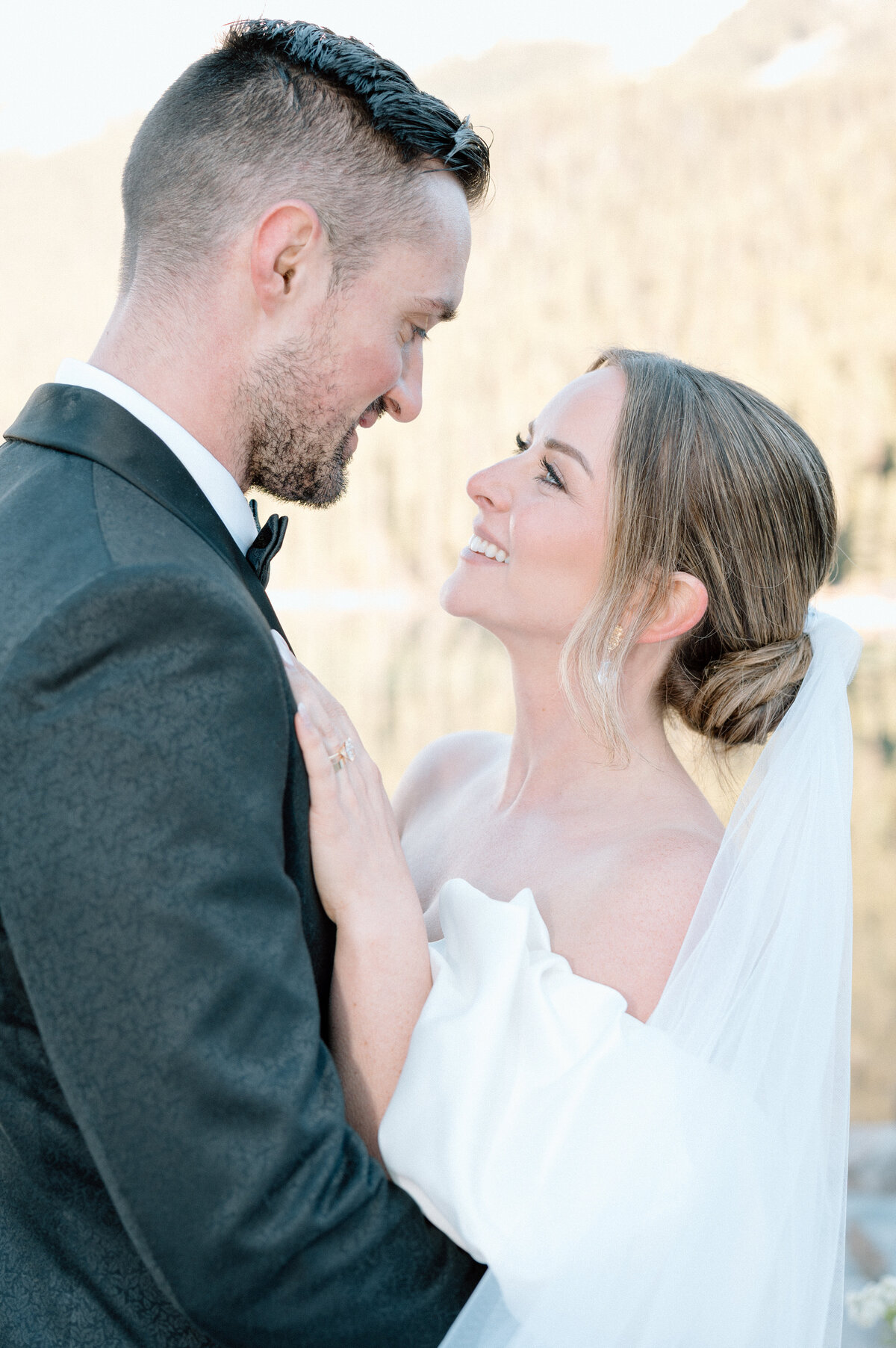 Bride and groom smiling at each other with rocky mountain backdrop