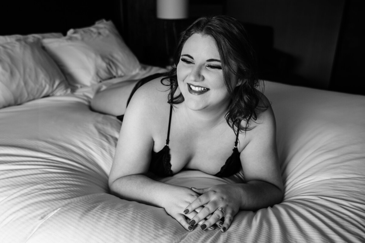 Black and white boudoir photo woman smiling on bed
