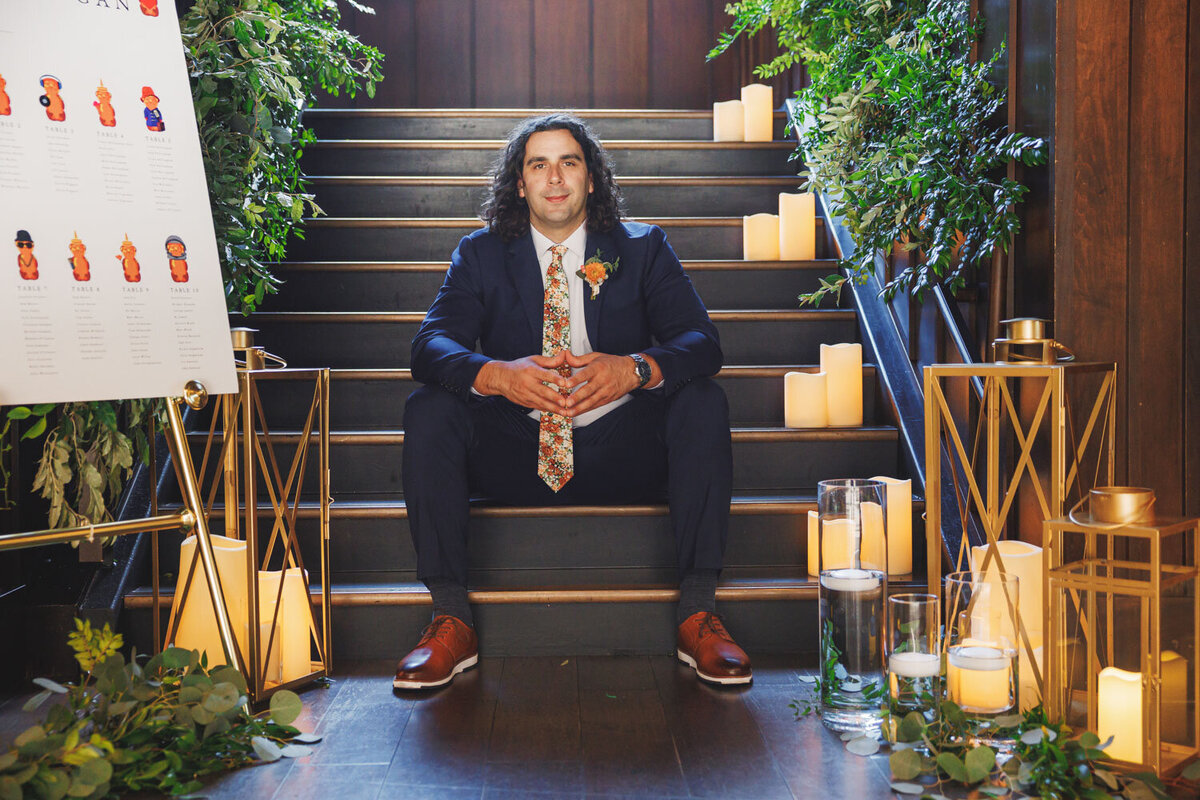 Groom sitting on the staircase with greenery and candles
