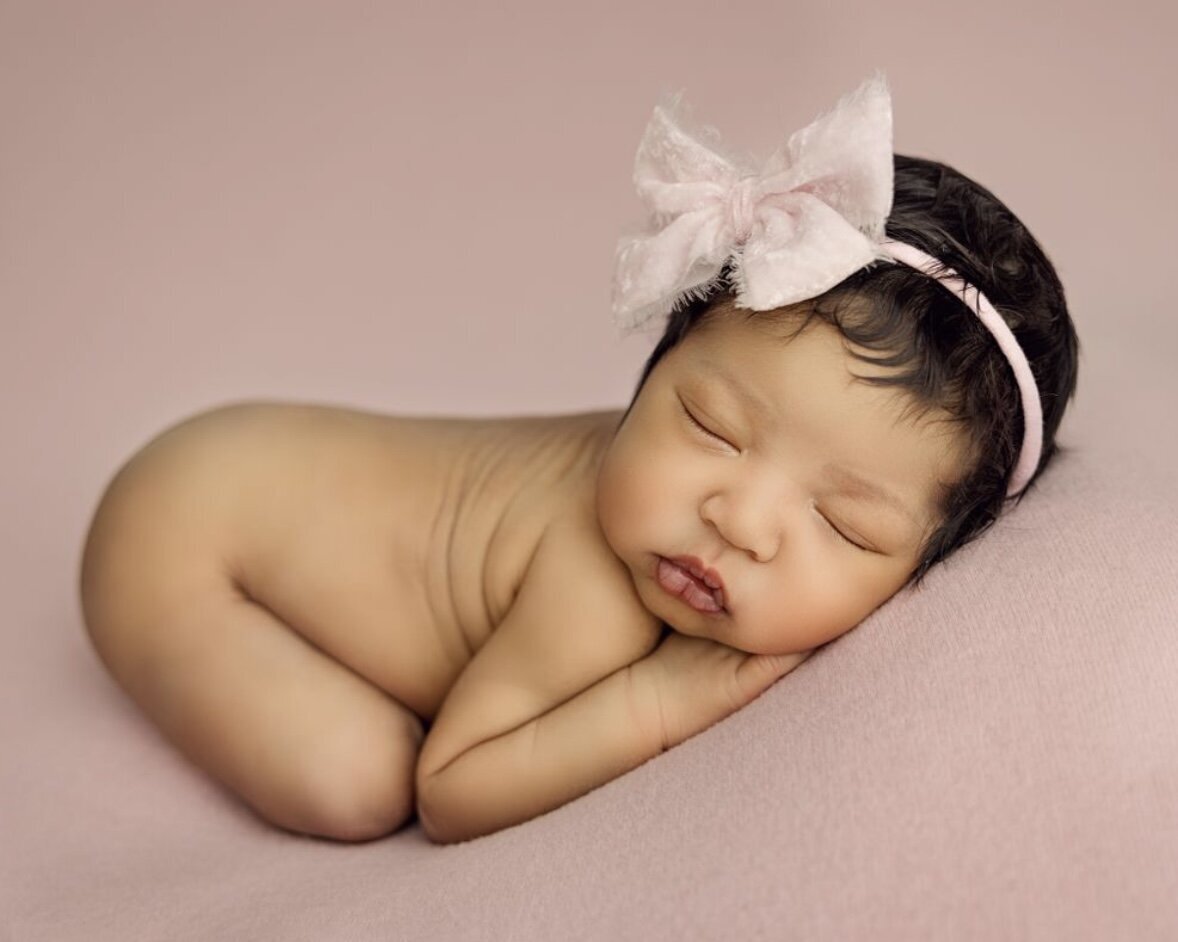 3 weeks baby girl lying on pink blanket and posed bum up wearing a pink headband.