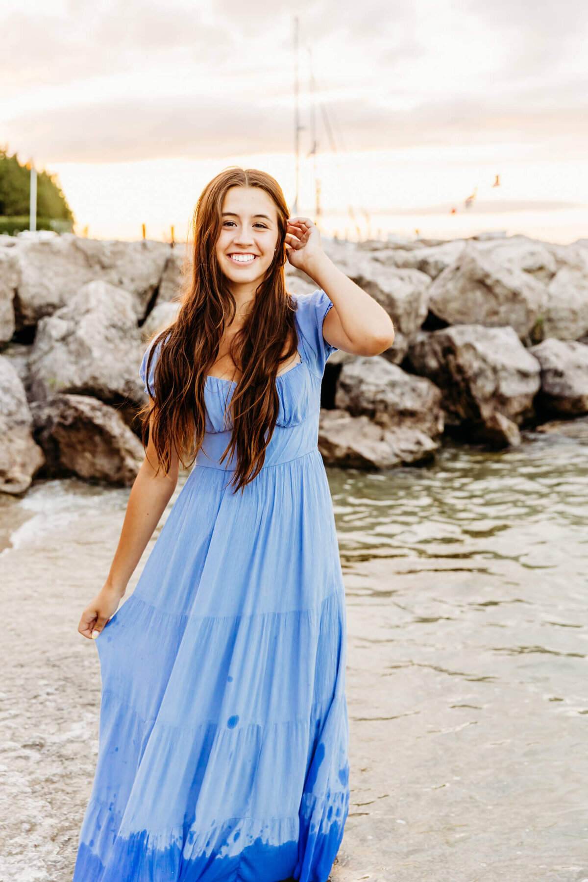 young lady in a light blue dress pulling her hair back as she walks along the beach