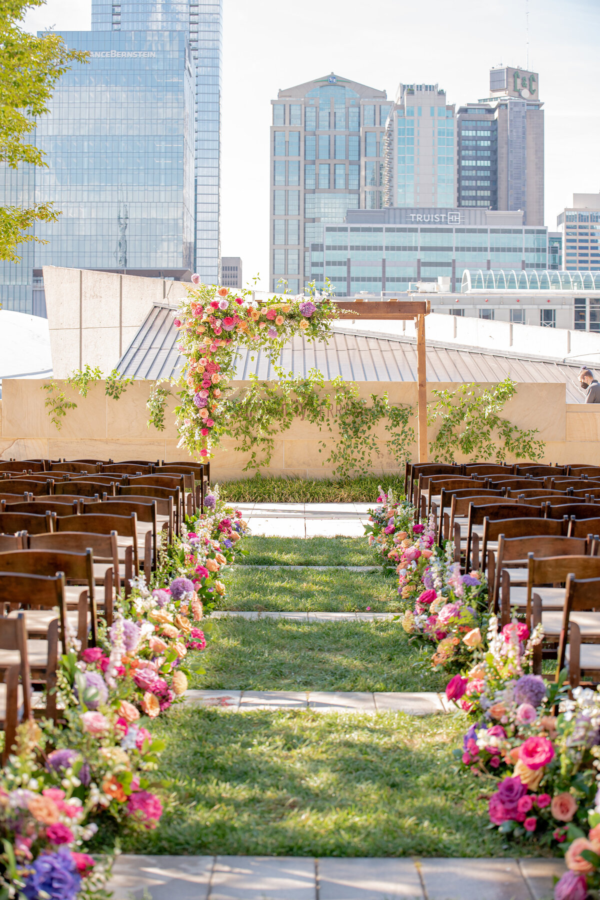Lush aisle markers filling the ceremony with sunset hues of pink, fuchsia, lavender, and orange composed of petal heavy roses, snapdragons, allium, hydrangeas and garden-inspired greenery. Design by Rosemary and Finch in Nashville, TN.