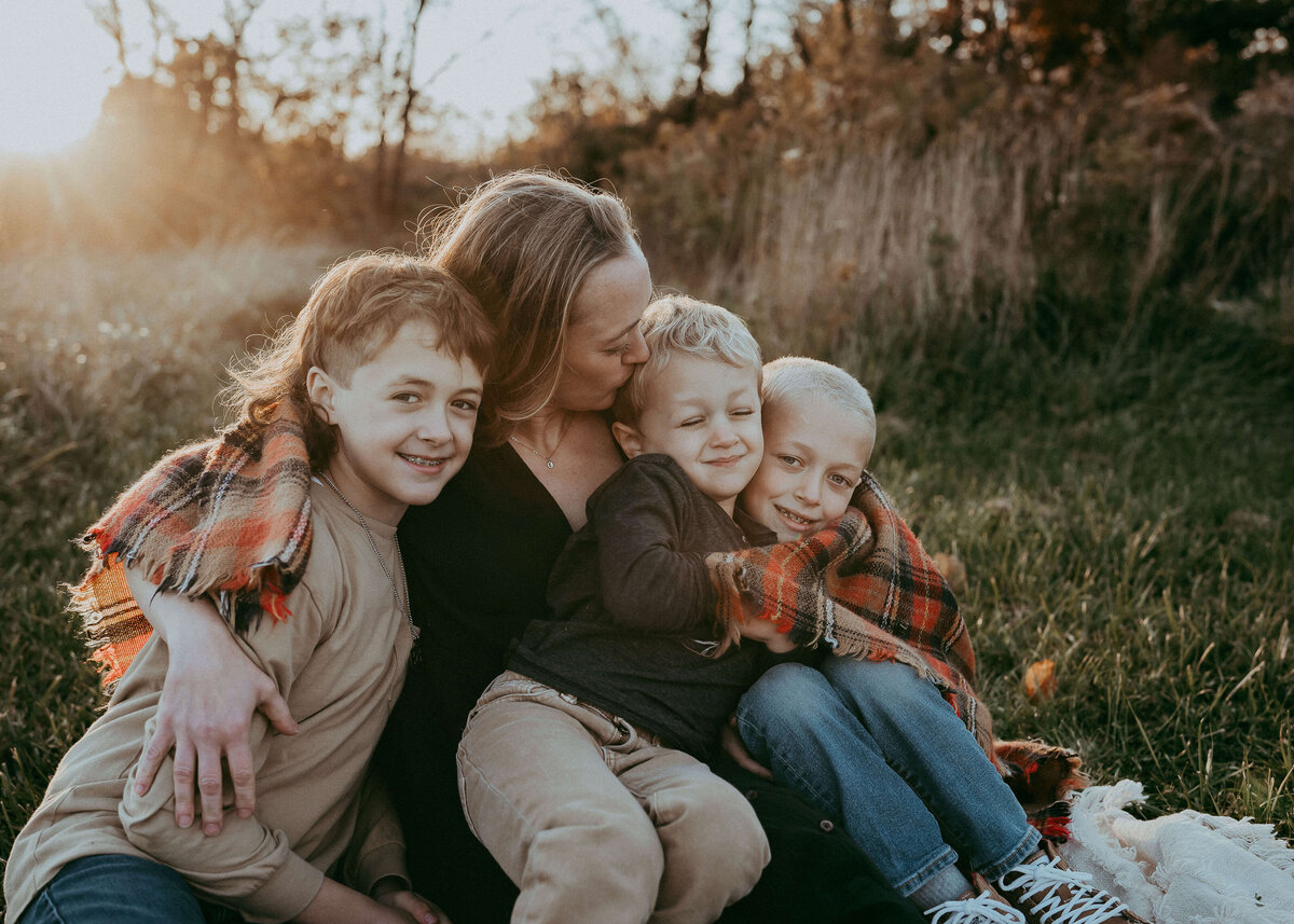 A gorgeous young mom cuddles her three boys lovingly during an outdoor family session.