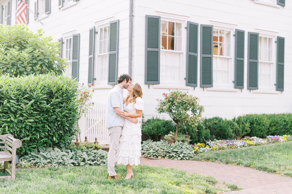 Couple kissing in front of a white home in old town Alexandria, by Rachael Mattio Photography