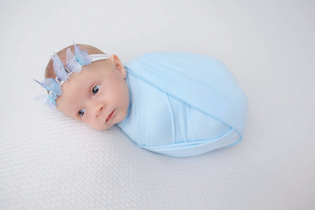 two week baby girl wearing a baby blue colored wrap and a matching butterfly headband posed at Heather Nicole Photography.