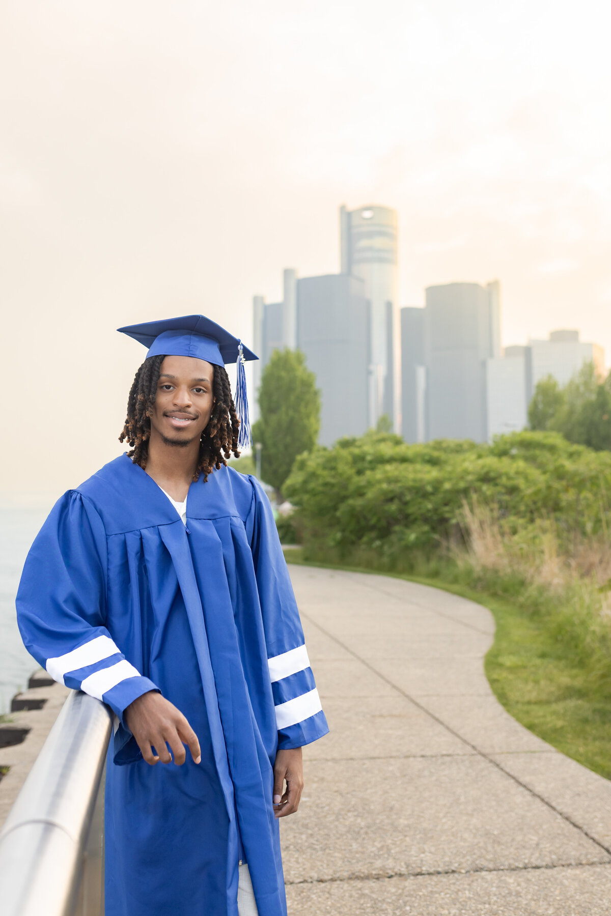 Senior boy posing for downtown Detroit senior photos on Detroit River walk wearing cap and gown