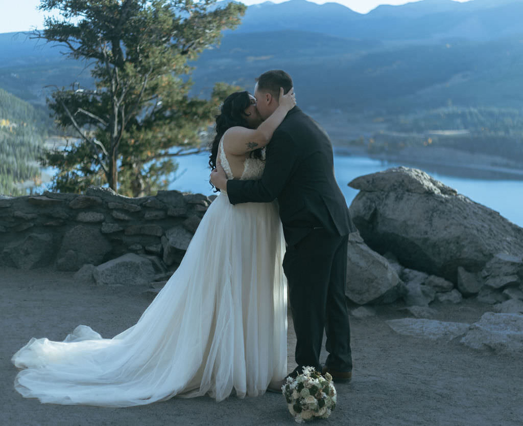 A newlywed couple kissing with a bouquet of flowers at their feet.