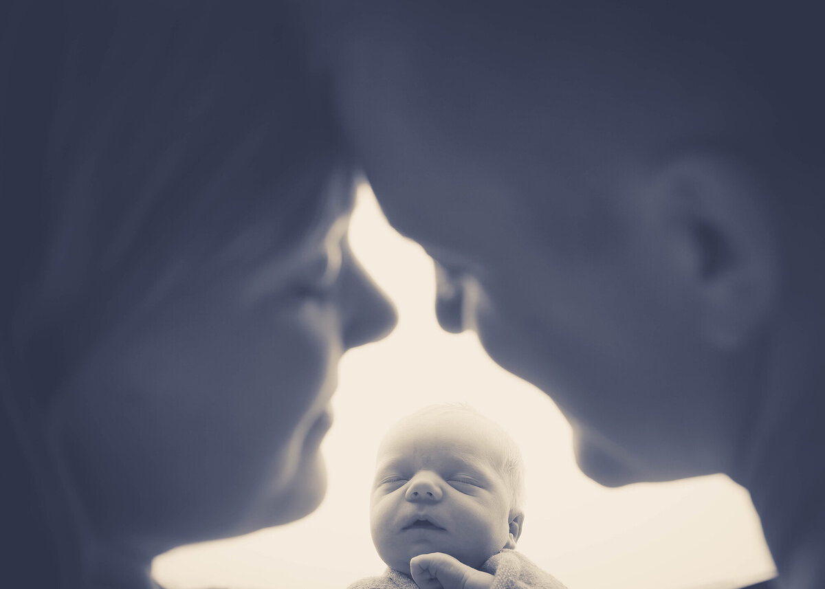 Happy parents snuggle foreheads over their sleeping newborn in their hands