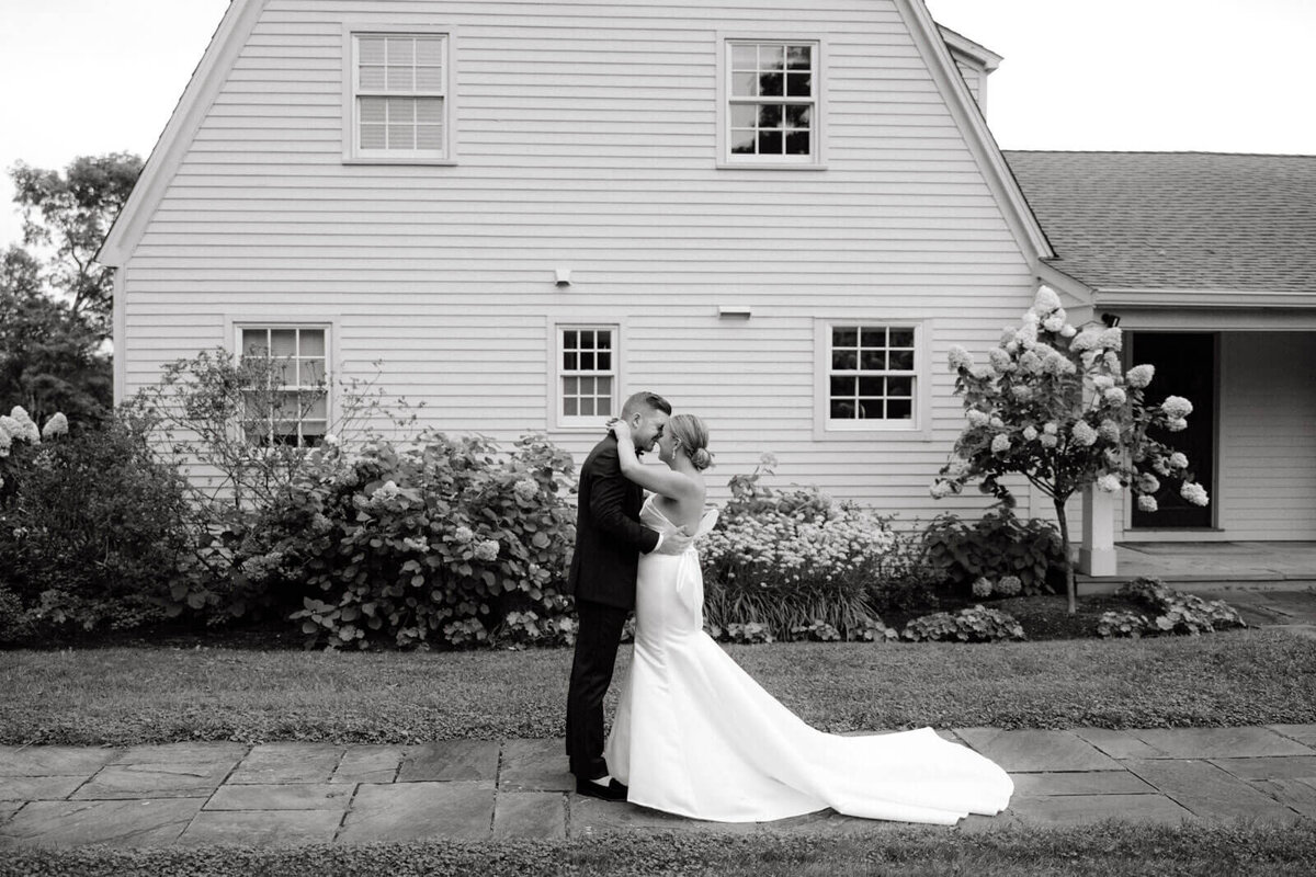 The bride and groom are romantically standing close outside the guest house at Lion Rock Farm, CT.  Image by Jenny Fu Studio