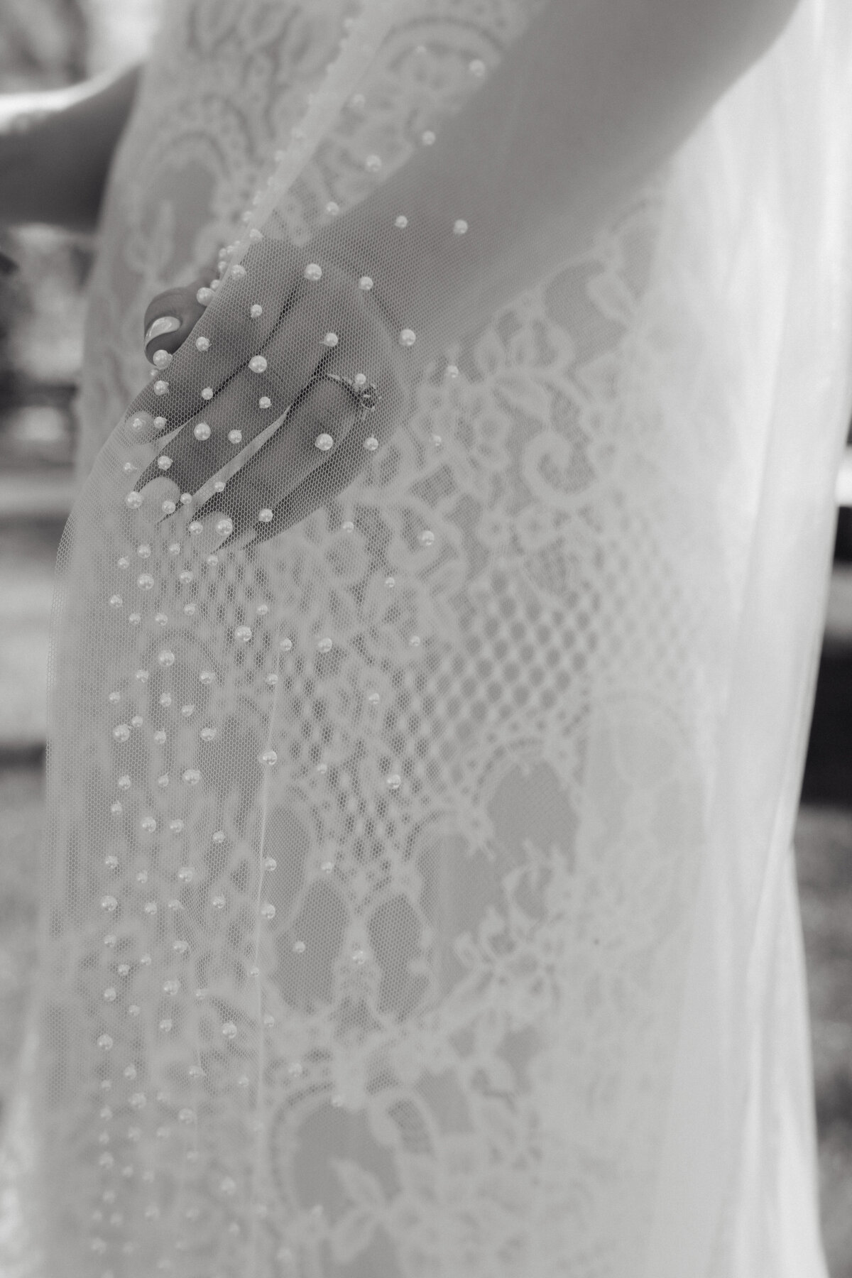 Close-up of bride's delicate pearl-studded veil and lace wedding gown, highlighting intricate textures.