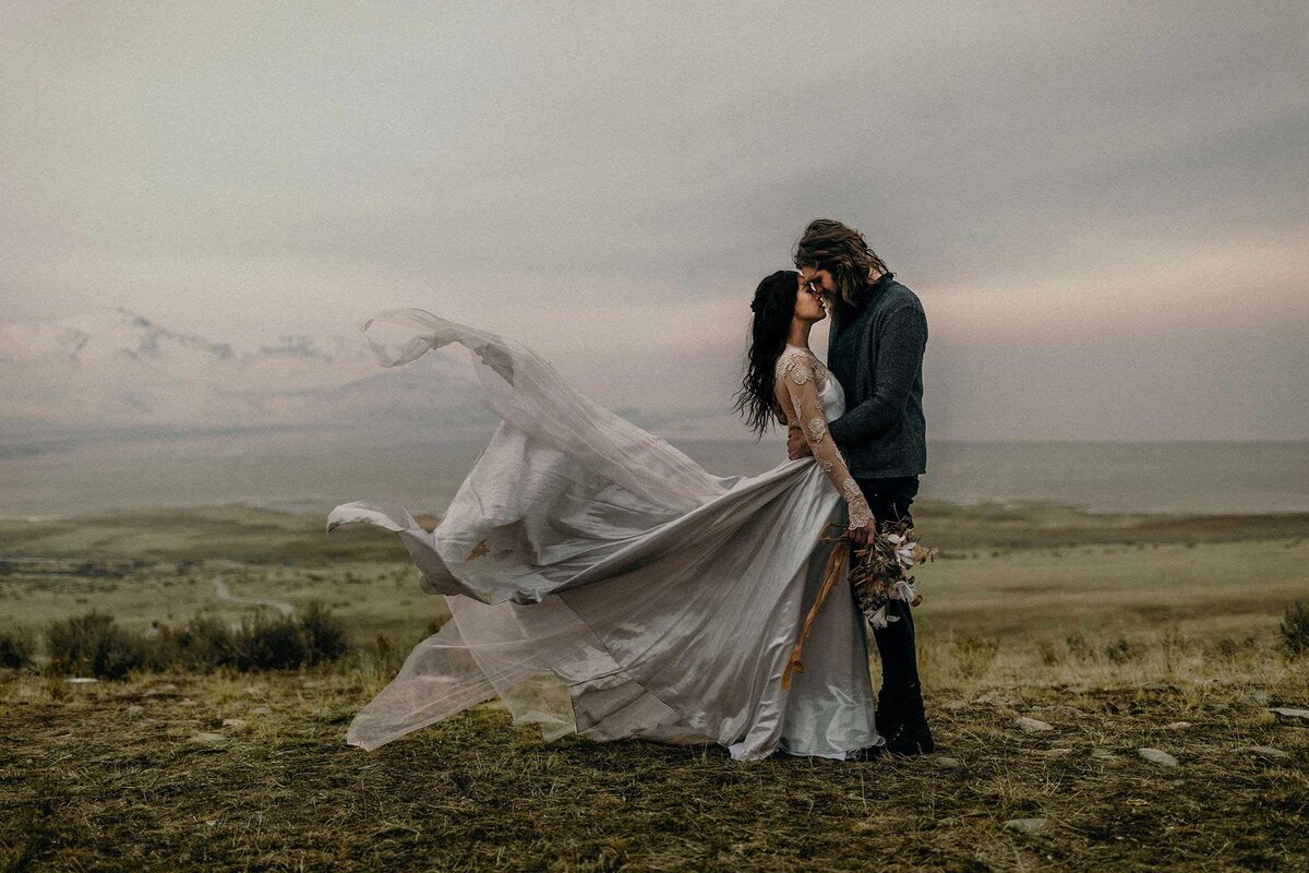 An eloping couple embracing in the highlands of Iceland. The bride's dress is blowing in the wind.