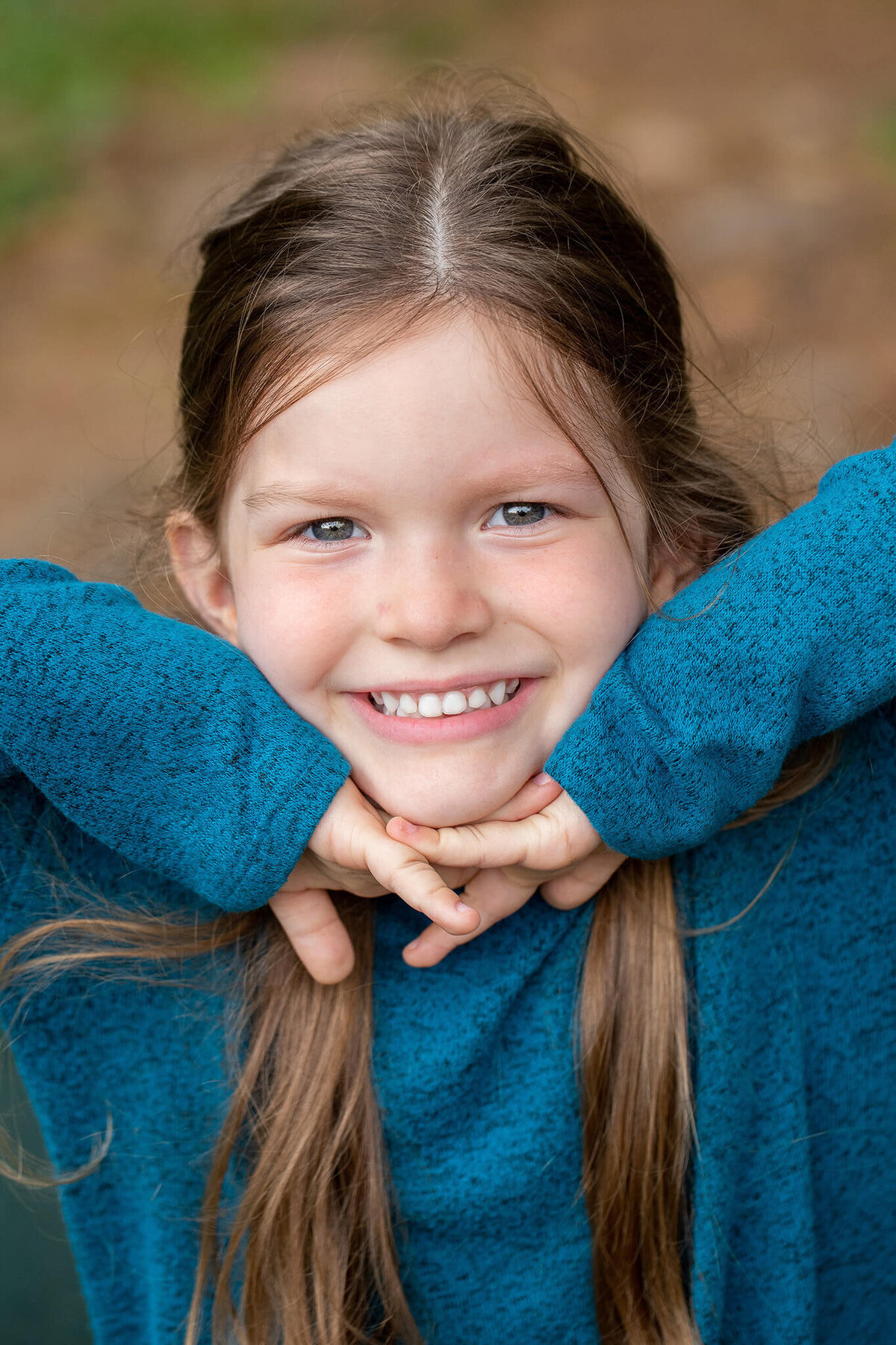 My daughter wearing a blue sweater and smiling with her hands under her chin.