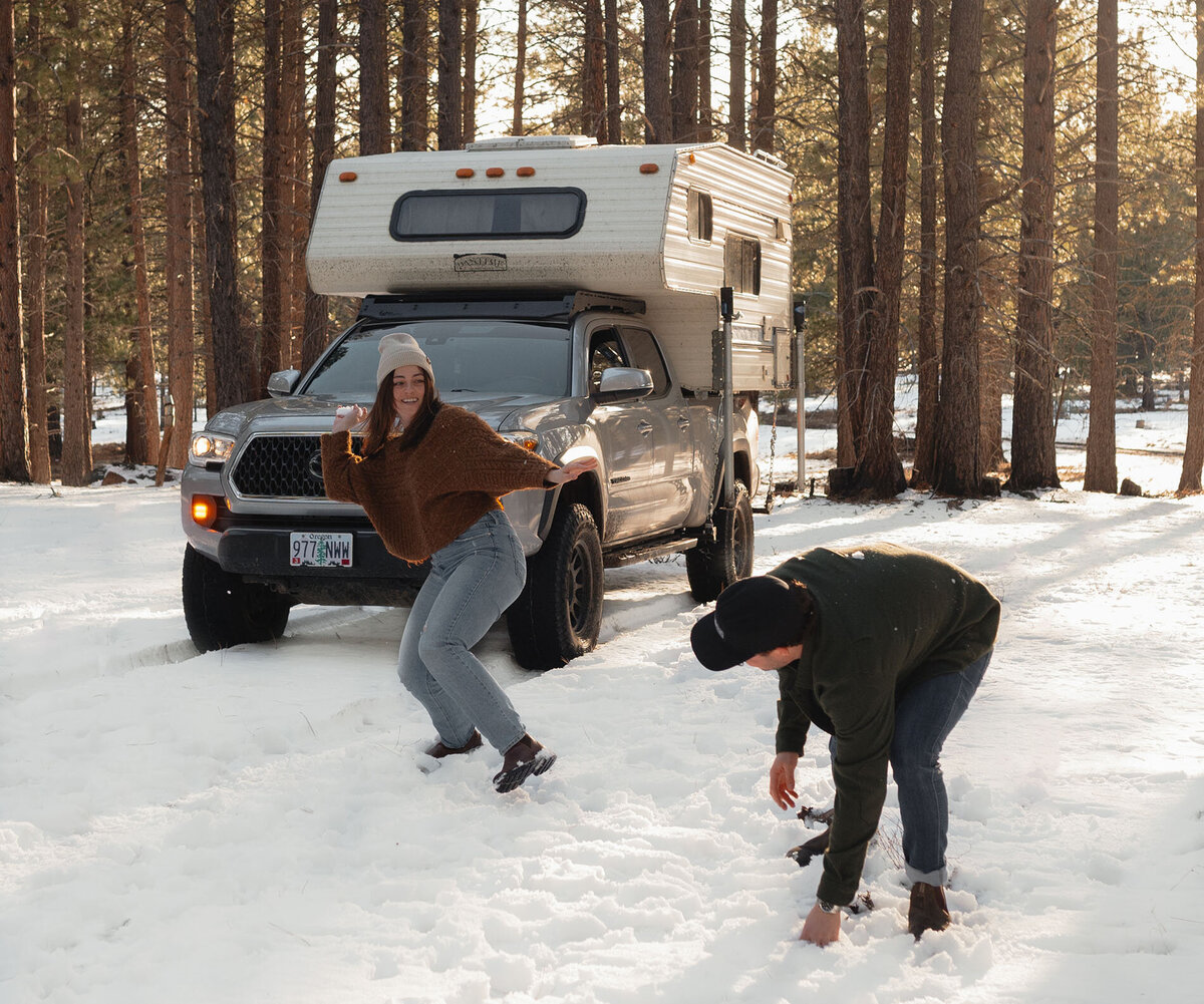 a couple throw snowballs at each other with their truck and camper in the background during a snowy elopement in Bend, Oregon