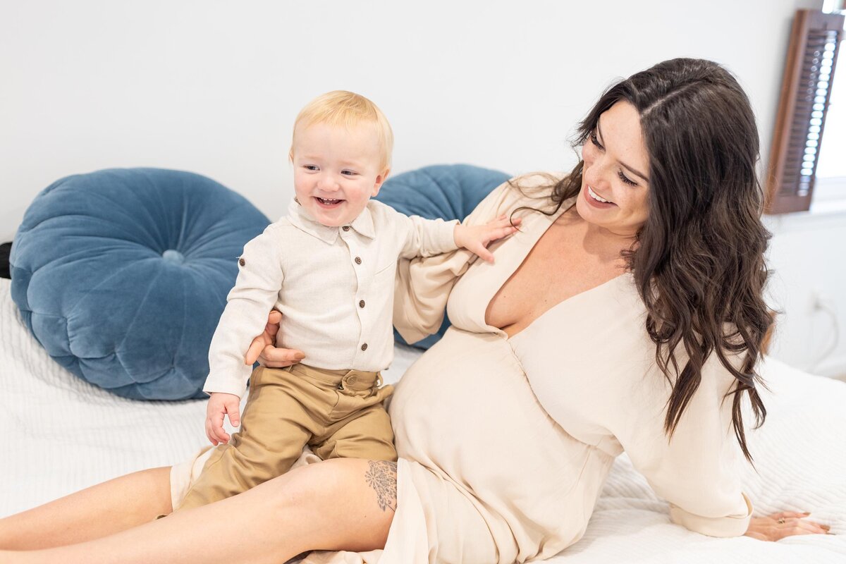 In-home Virginia Beach Maternity Photo of a Pregnant Mother sitting on the bed holding her 1 and a half year old playing by Mary Eleanor Photograhy