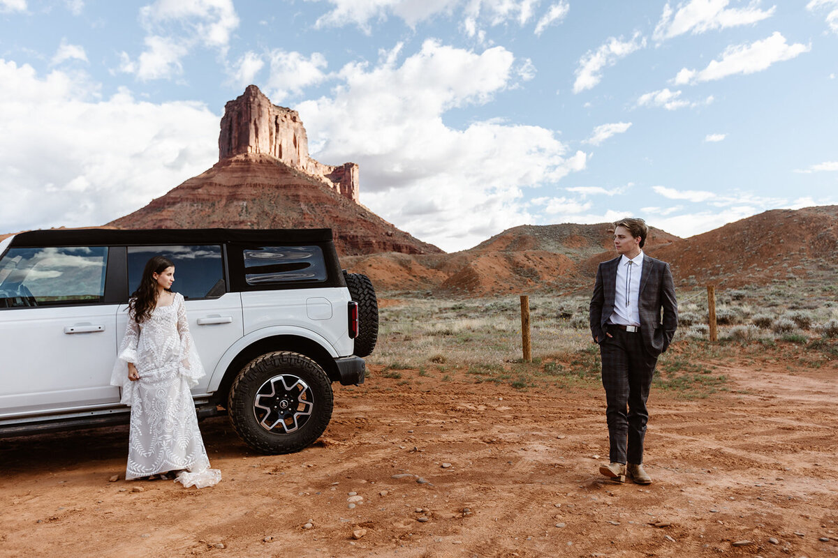 A couple stands in front of sone giant red rock formations, and their Ford Bronco in front of Ida Gulch trails before their elopement. 