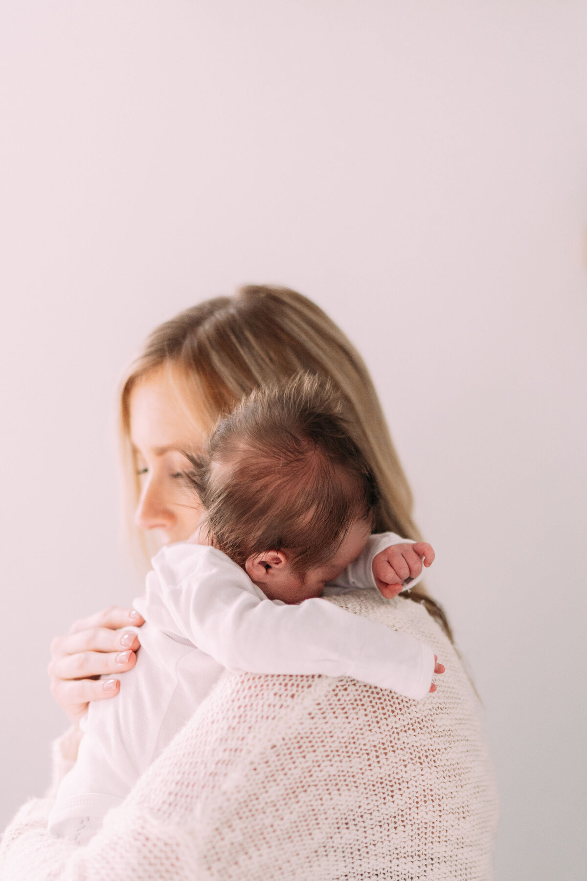 mother holds baby boy with fluffy hair over shoulder