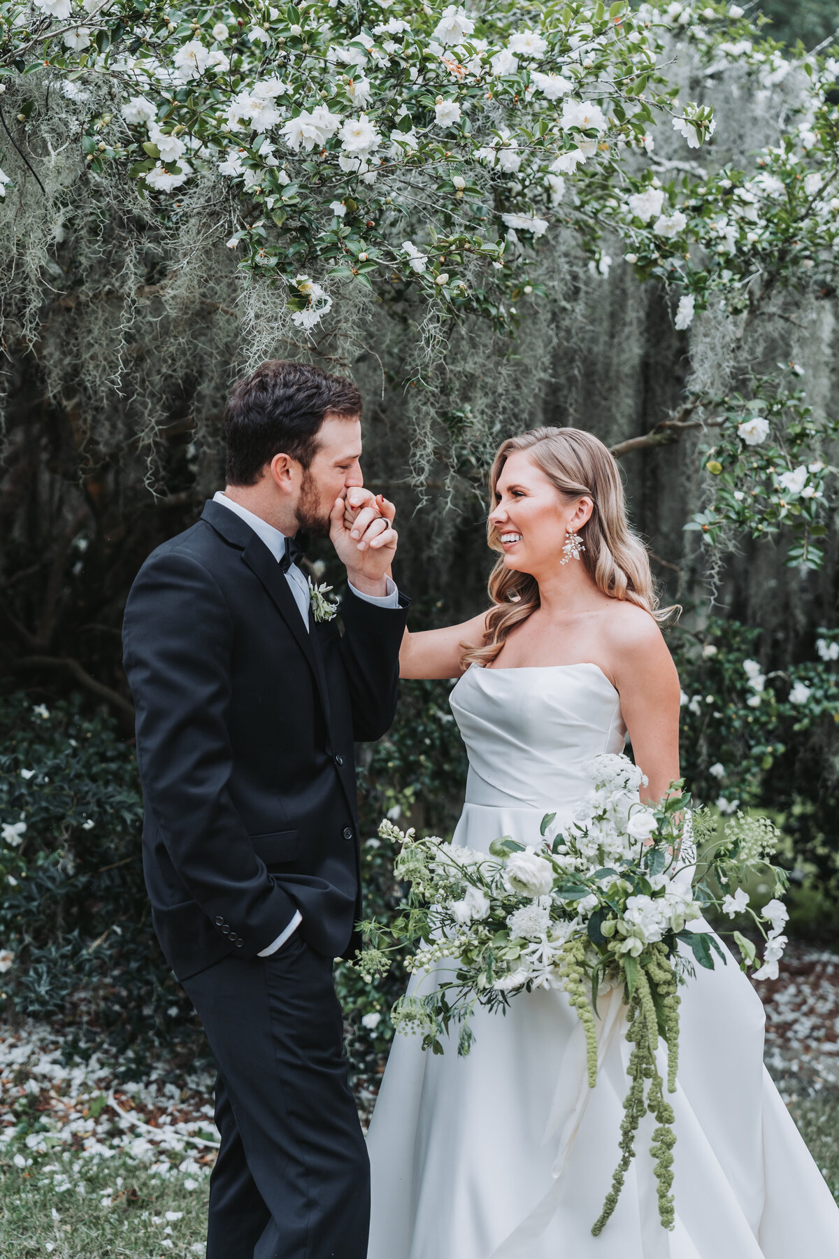 Groom kisses bride's hand under flowered tree