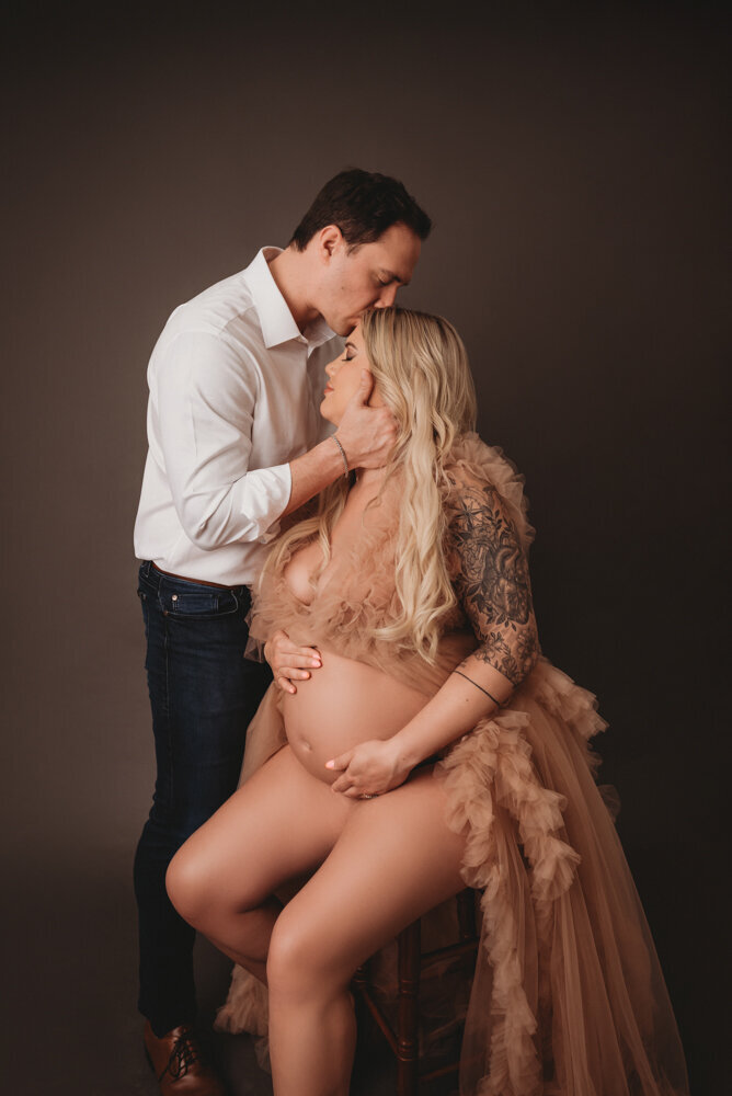 Atlanta, Georgia maternity photographer high end maternity portrait session with Atlanta maternity and newborn photographer. Pregnant woman in rose color tulle ruffle dress standing with her husband holding her tummy.