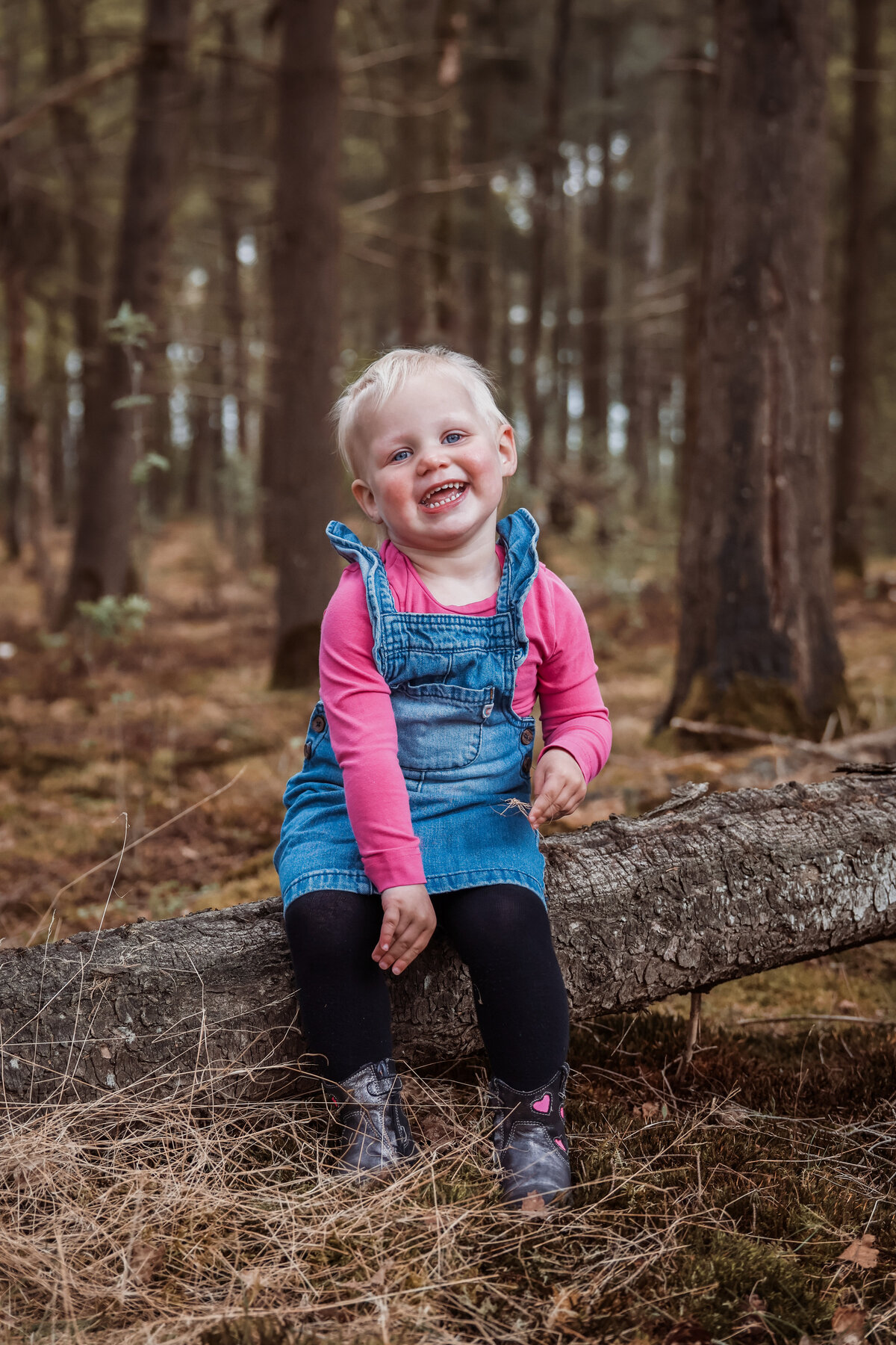 Meisje lacht en zit op een boomstam in het bos.