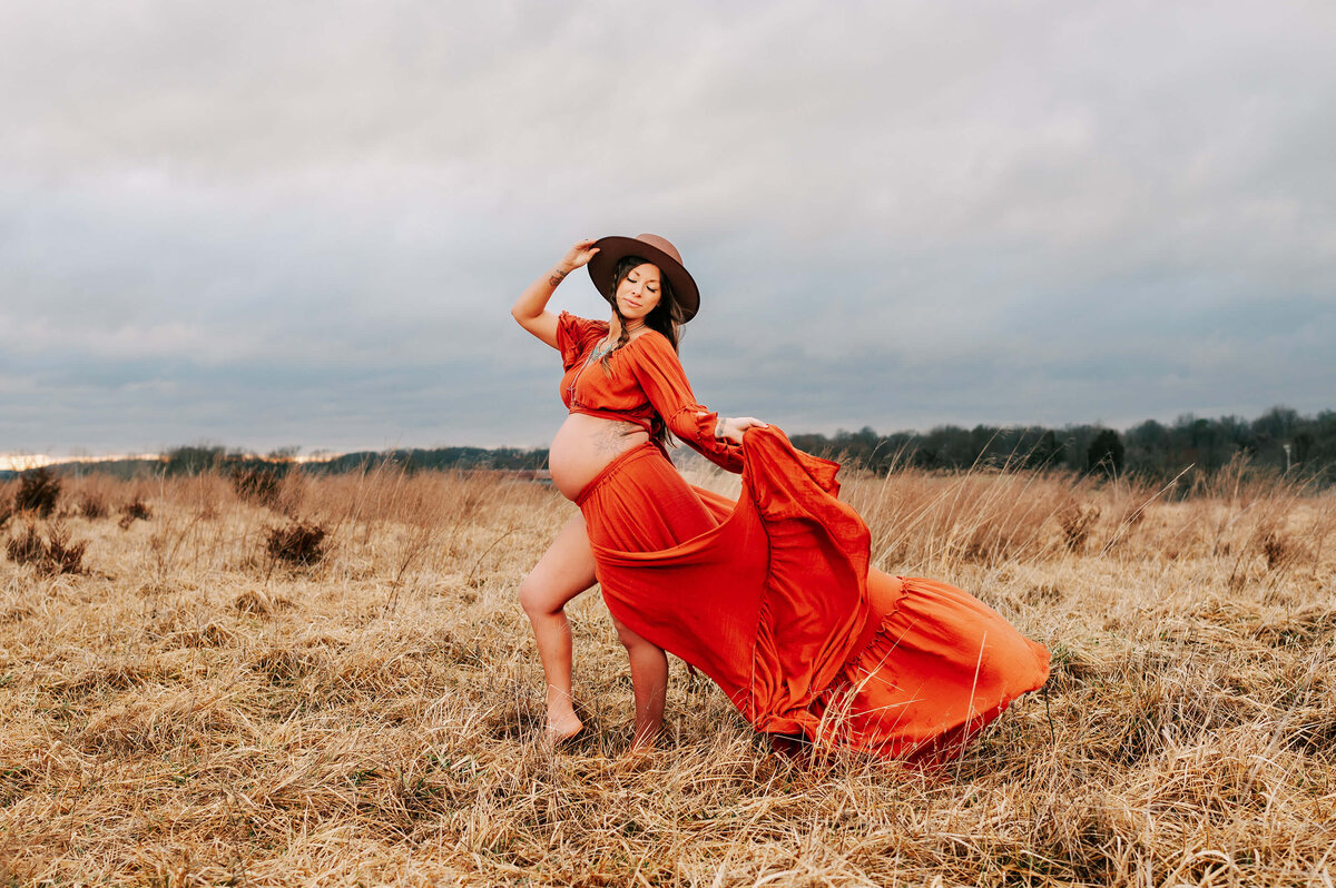 Springfield MO maternity photographer Jessica Kennedy of The XO Photography captures pregnant mom holding her hat and skirt walking in a field during a storm