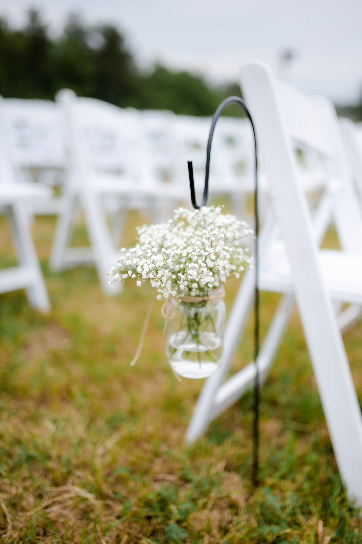 white fold up chairs lined up for wedding ceremony with white babies breathe in a mason jar