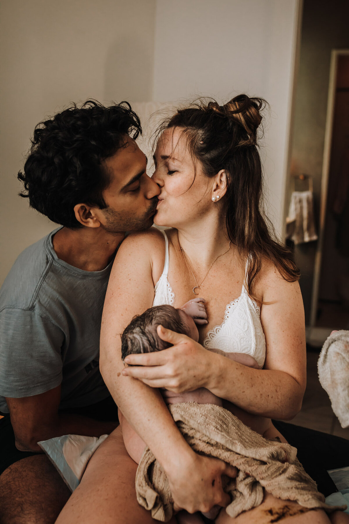 man and woman kissing holding newborn