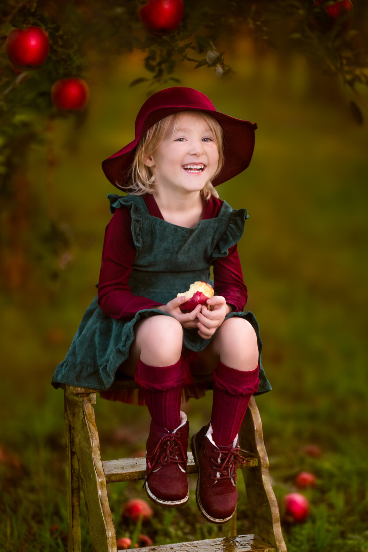 Delightful portrait of a young girl dressed in fall attire, sitting in an apple orchard with a charming vintage setup. Captured in Gardner, Kansas, this cozy scene is perfect for autumn-themed child photography in the Kansas City metro area.