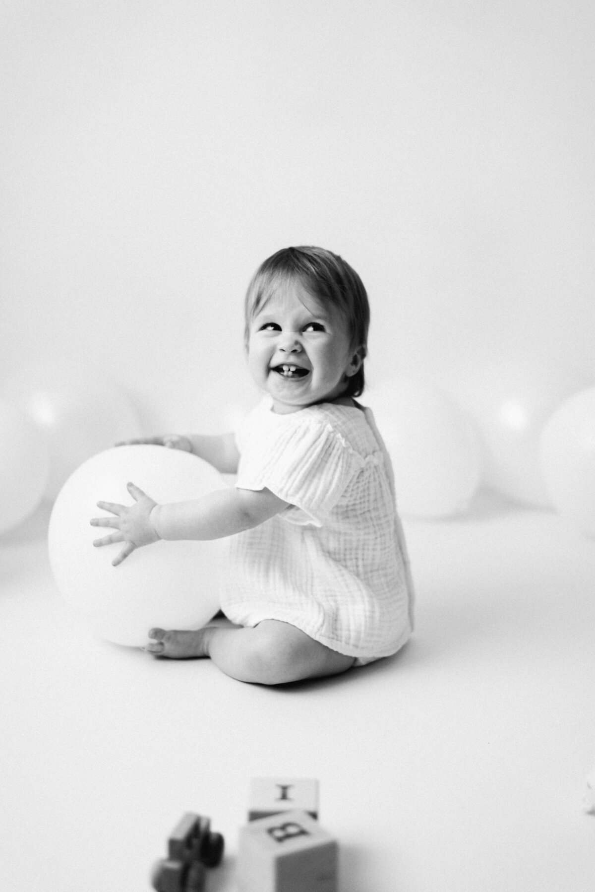 Baby girl sitting on the floor holding a balloon and laughing at a cake smash photoshoot in Billingshurst