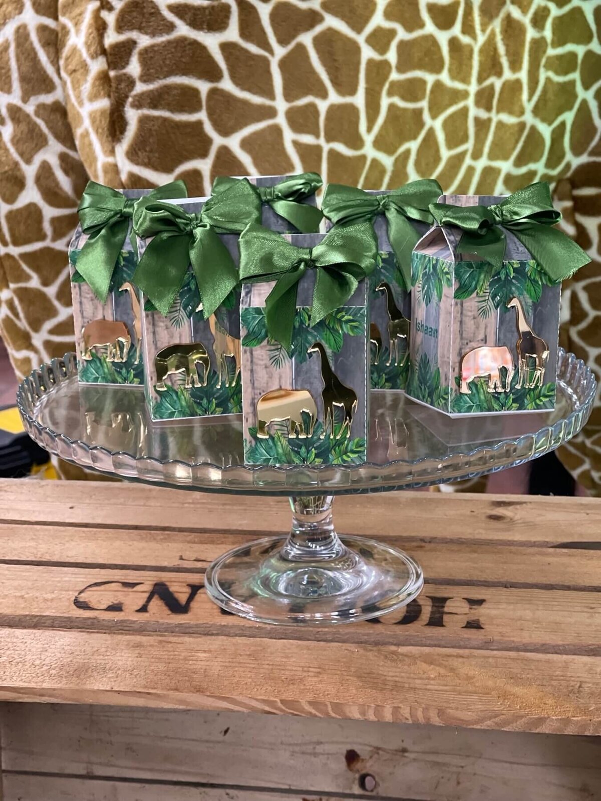 Children's jungle themed gift boxes with green silk ribbon on a glass cake stand with a giraffe backdrop