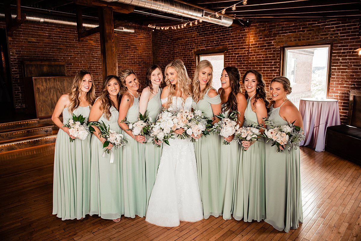 Bridesmaids wearing a soft mint color standing grouped around bride with brick walls surrounding them