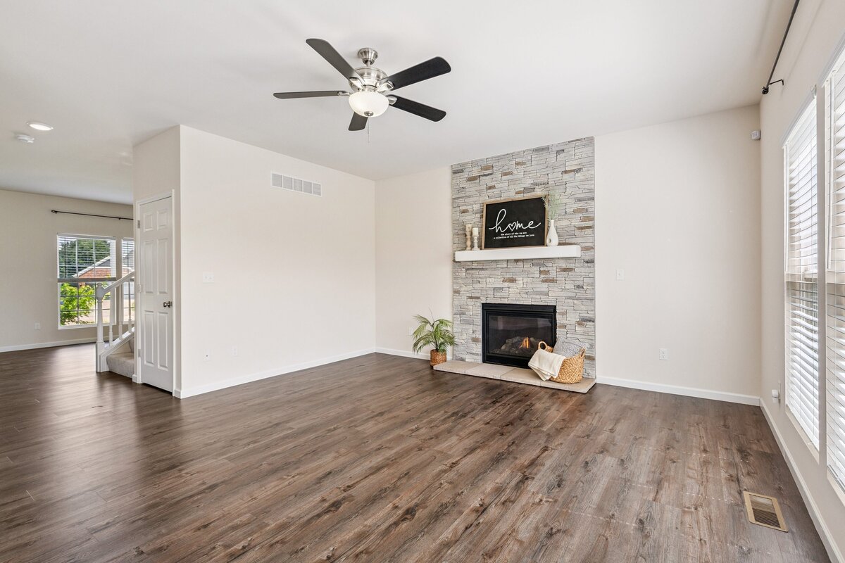 Real estate listing photo of the living room of a home, with brick fireplace and painted wooden sign above the fireplace.