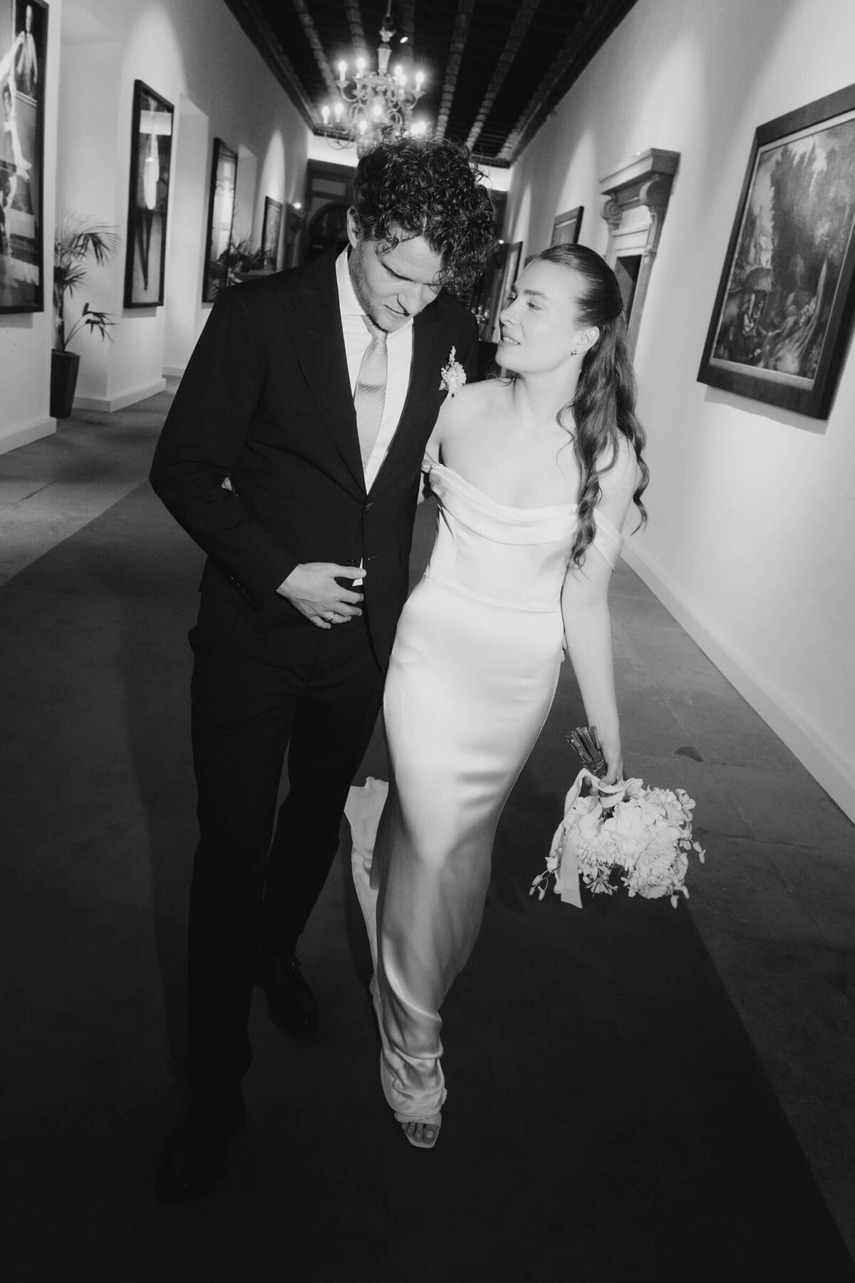Brautpaar schreitet durch Galerie – Hochzeit im Palast Hohenems mit künstlerischer Atmosphäre.

