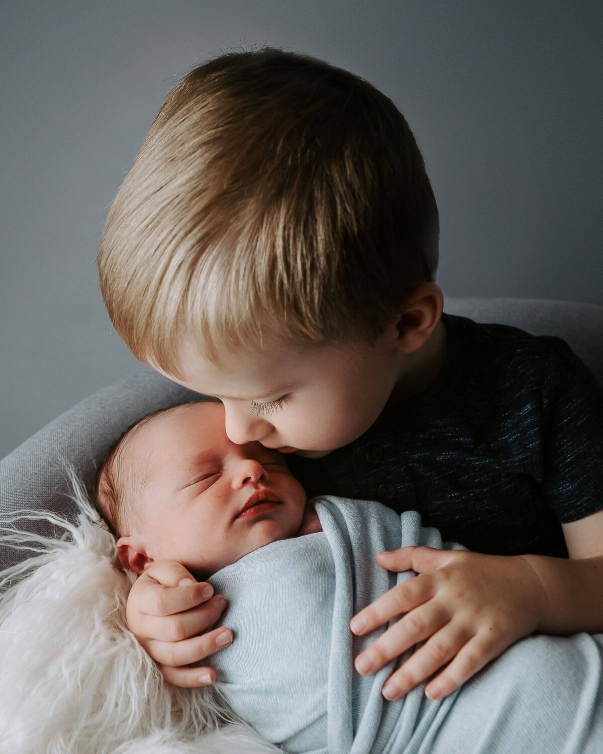 A boy kisses a newborn baby boy captured by a Pittsburgh newborn photographer.
