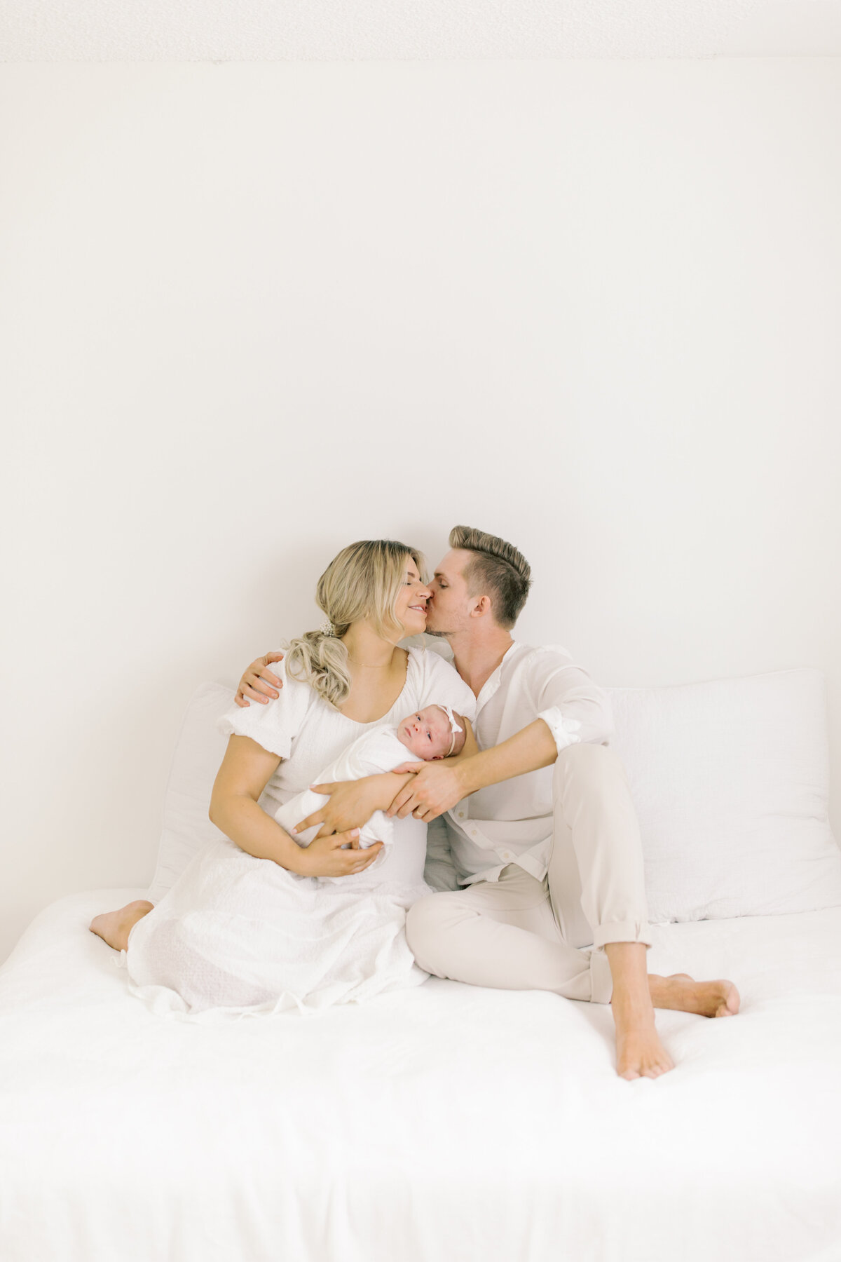 newborn photography spokane wa image of mom and dad kissing and holding newborn baby in studio spokane