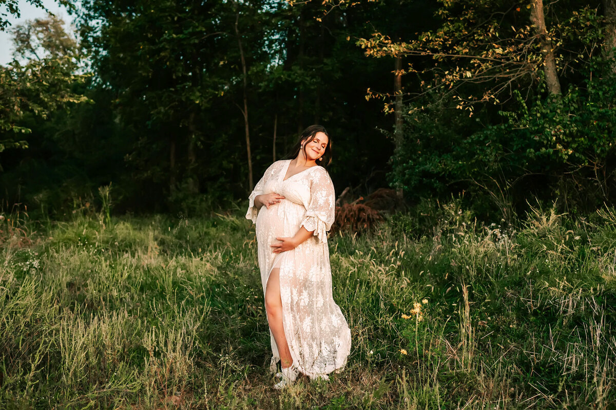 pregnant mom holding baby bump at sunset in a field outdoors during Branson maternity photography session