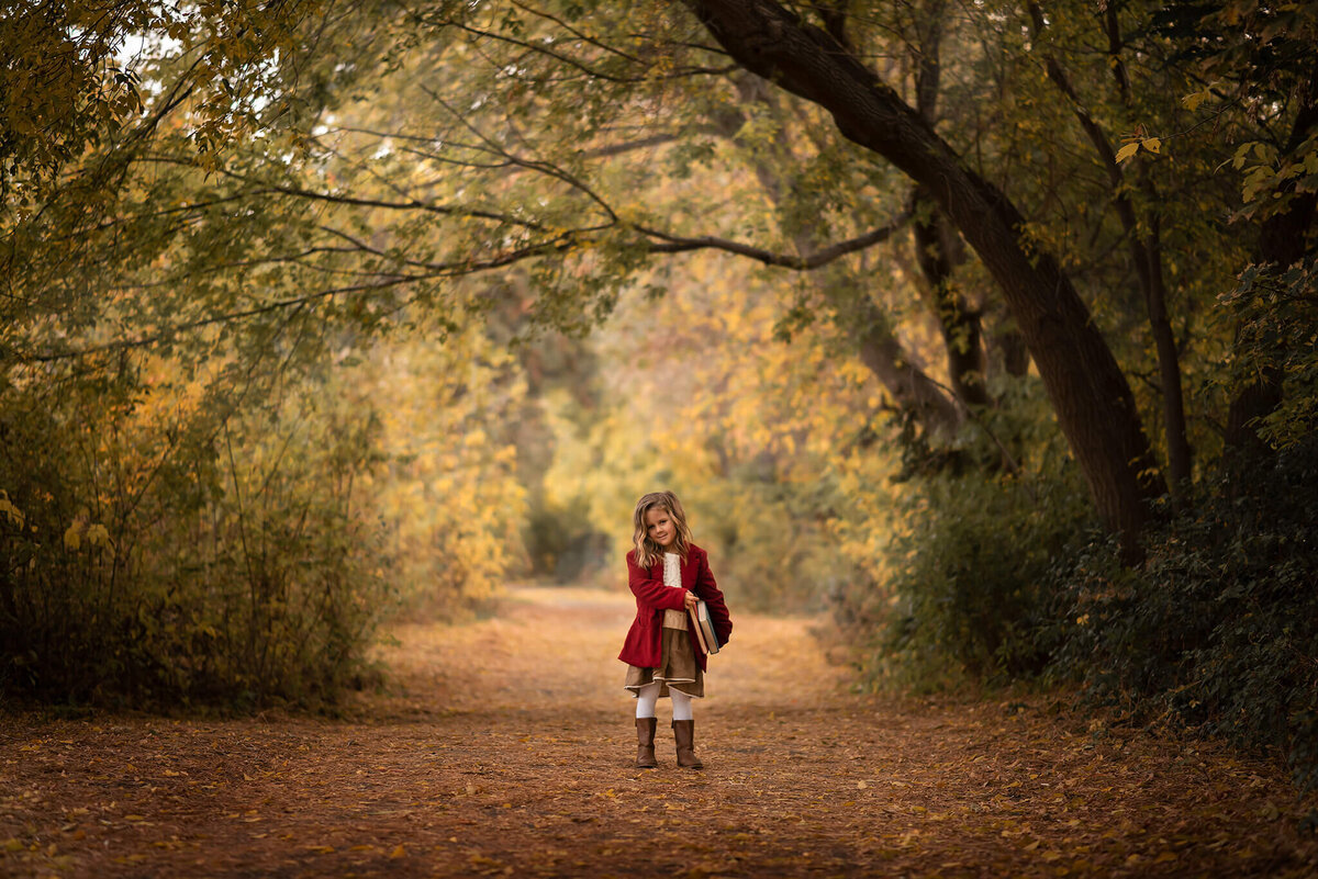 Brittany Danielle takes a gorgeous photo of a girl wearing a red coat. There is a large tree and beautiful fall background.