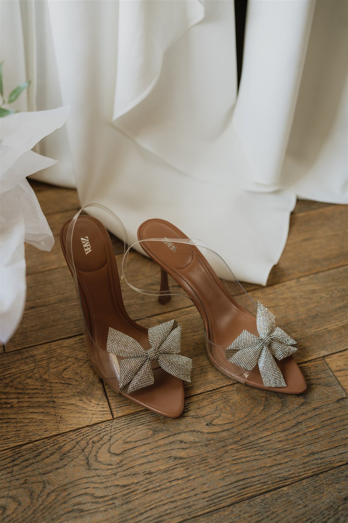 A pair of bridal shoes sit on the floor next to a wedding dress.