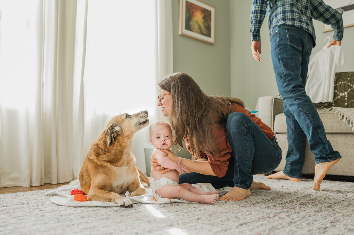 Mom holds her baby and smiles at the dog in their San Antonio nursery.