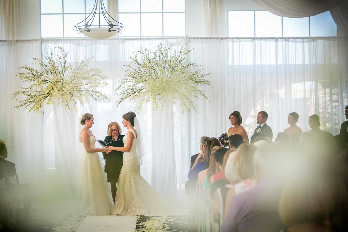 two bride getting married under tall white flower arch