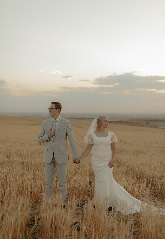 A bride and groom pose for bridal portraits for their wedding. They're standing next to each other with a little gap in between them holding hands.
