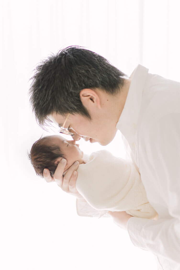 パパと鼻を合わせている赤ちゃんの姿が美しい、ナチュラル・ニューボーンの写真。逆光でYukika Ishikawa Photographyが撮影。