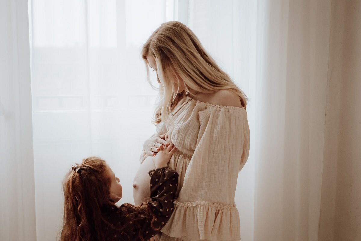 Sensuele zwangerschapsfoto in zachte natuurlijke lichtinval vrouw met dochtertje pure vrouwelijkheid