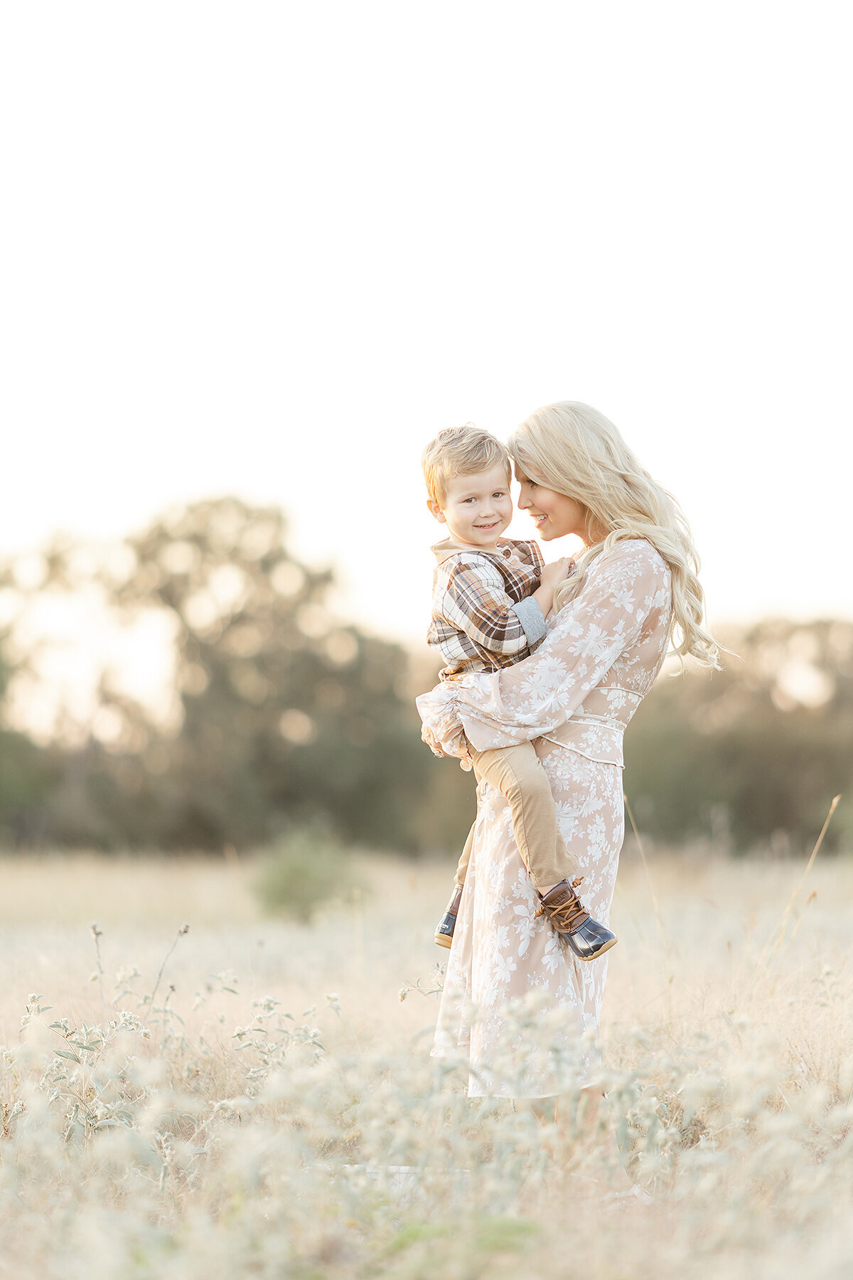 A mother holding and her toddler son while he smiles and looks away at their family photographer.