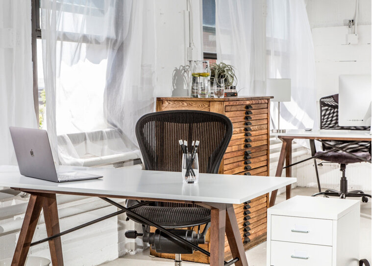 an office with a desk & chair in front of a cabinet & windows with white sheer drapes taken by a South Shore MA branding photographer