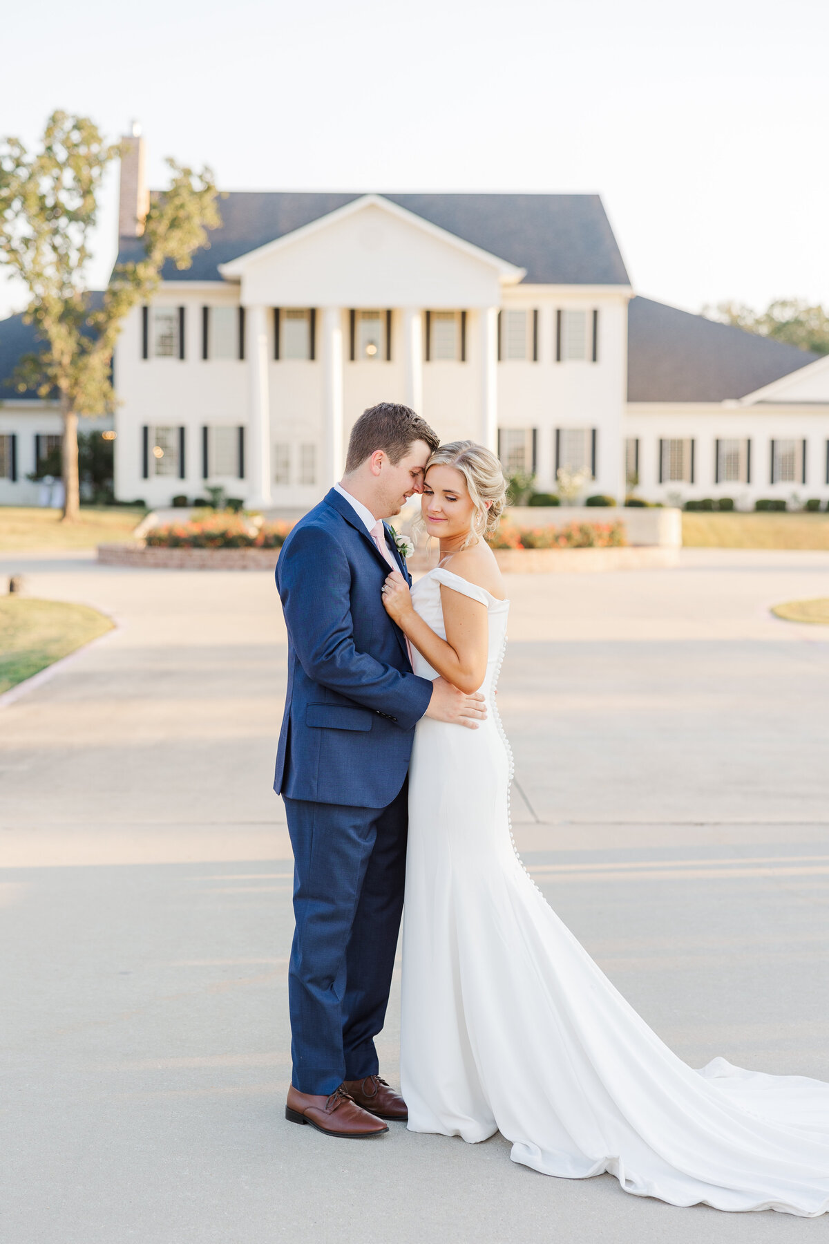 Bride and groom share a quiet embrace in front of a stately Southern mansion, highlighting a graceful moment of connection in Denton.