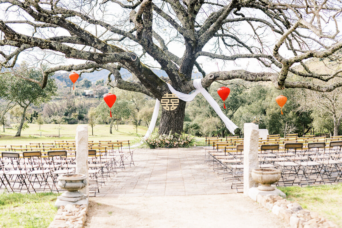 walnut tree at napa wedding ceremony venue with floral grounded arch installation and white linen draping under double happiness sign and lanterns