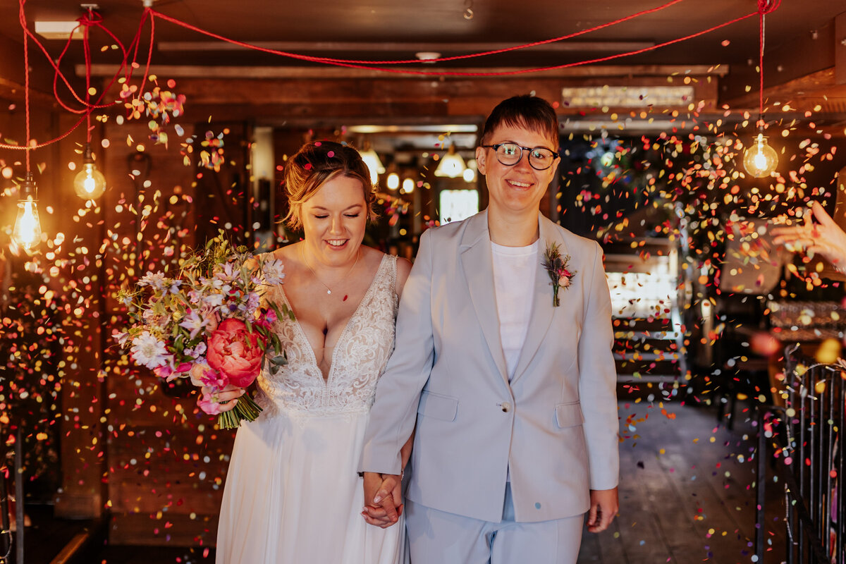Two brides walk under a tunnel of confetti at The Bell in Ticehurst